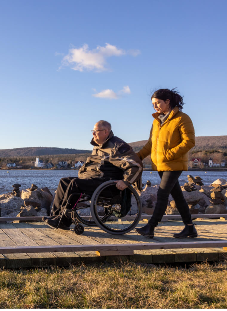 Woman walking elderhy man in wheel chair on a dock