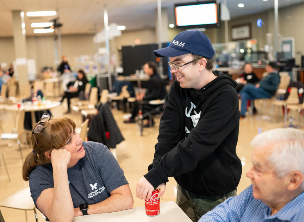 Person holding can of coke while talking to someone at a table